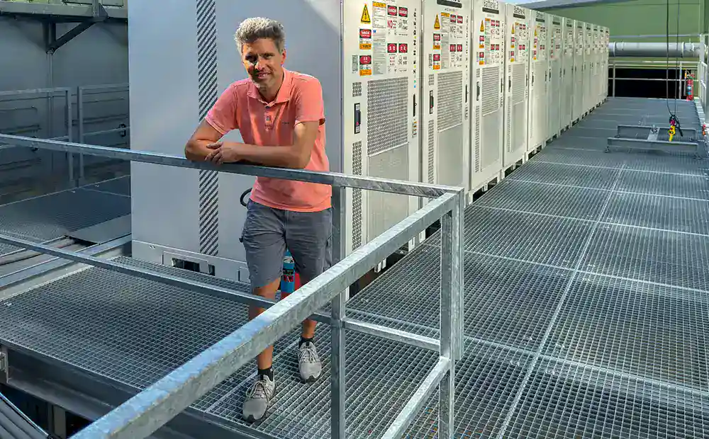 Ein Mann in sommerlicher Kleidung steht vor 12 Batteriespeicher-Modulen